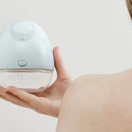 A nursing mother holding a handsfree wearable breast pump