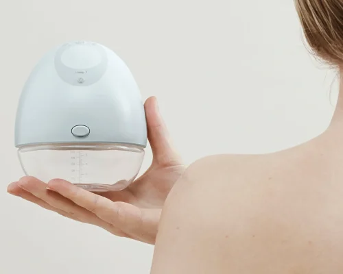 A nursing mother holding a handsfree wearable breast pump